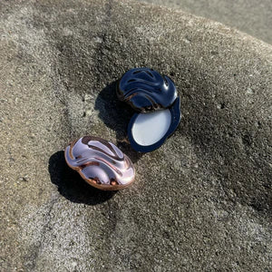 Two solid perfume cases with swirling patterns on a rock surface