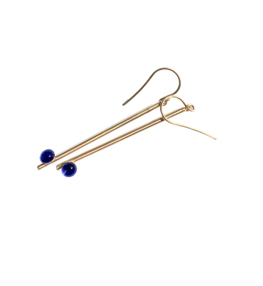 A pair of gold-toned drop earrings with slender bars ending in small dark blue beads, shown on a plain white background.