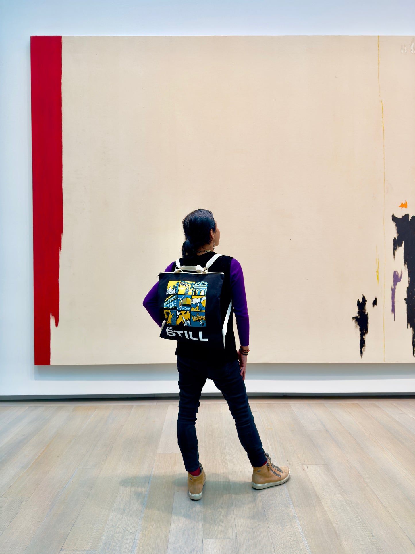 Person wearing a backpack with colorful design in front of a large abstract painting in an art gallery.