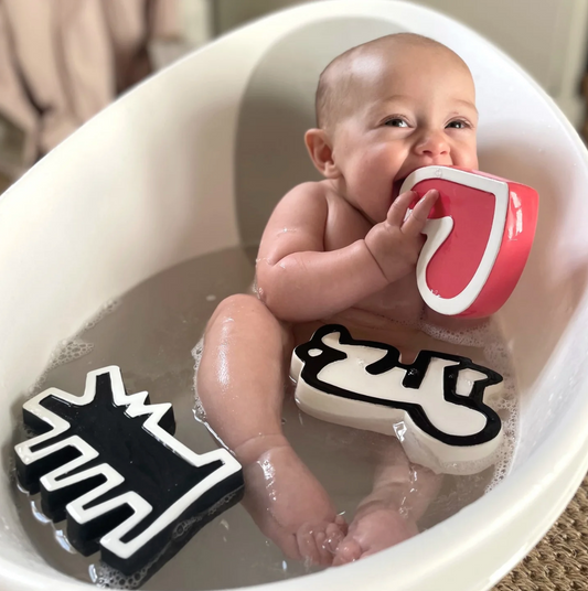 Photo showing baby sitting in bathtub playing with rubber Keith Haring bath toys.