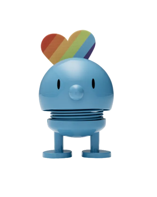 A colorful figurine with a round body and a rainbow-patterned heart on top, standing upright on a flat surface.