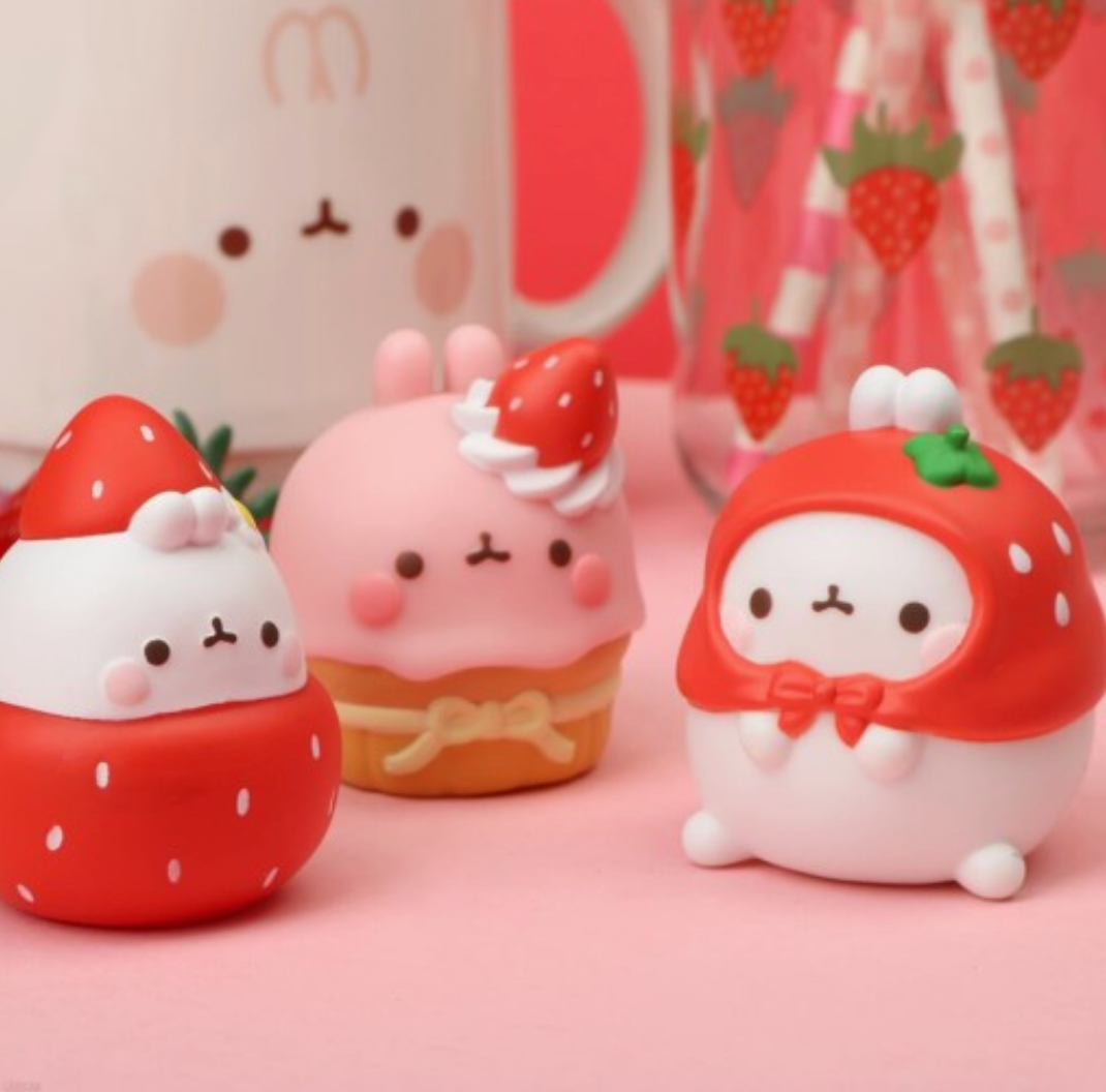 Three cute strawberry-themed figurines on a pink background.