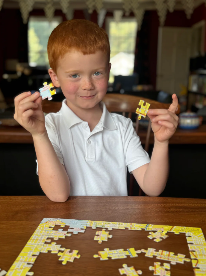 Child holding puzzle pieces with a completed puzzle on a table