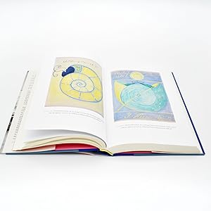 An open hardcover book with two illustrated pages spread open, photographed on a clean white background. The pages show pastel artwork, including a spiral design on the left page and a circular design on the right page.