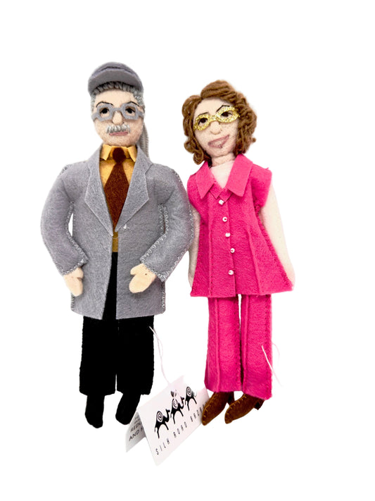 Two felt ornaments,  one in a gray coat and the other in a pink outfit, standing next to each other on a white background.