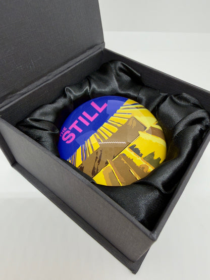 Colorful round paperweight with 'THE STILL' logo in a black box