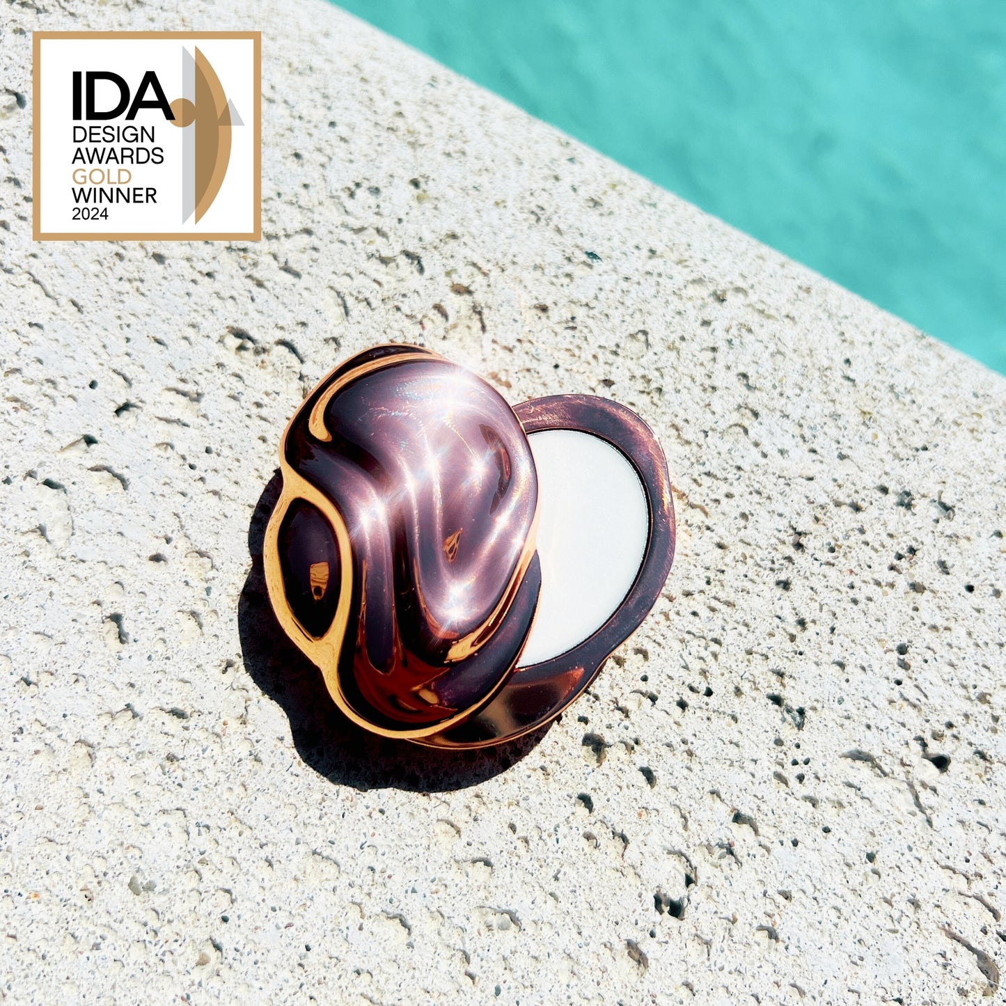 Decorative shell on a textured surface with a pool in the background, featuring the IDA Design Awards logo.