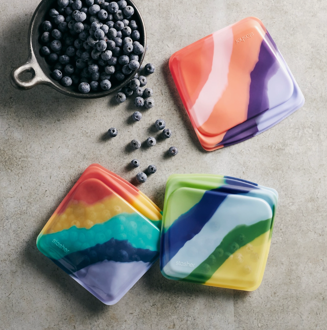 Photo of three colorful reusable silicone snack bags holding blueberries. 