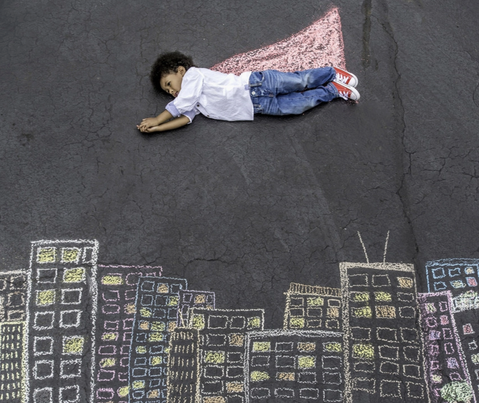 Image of young child lying on street with a chalk cape.