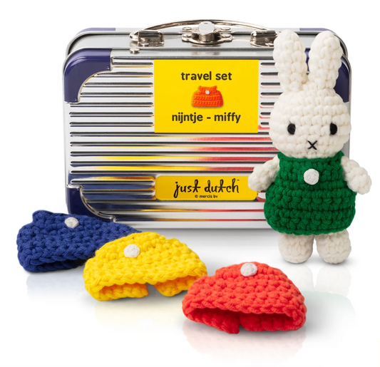 Crocheted dresses in blue, yellow, and red with a small Miffy rabbit figure in a green outfit in front of a striped suitcase labeled 'just dutch'.