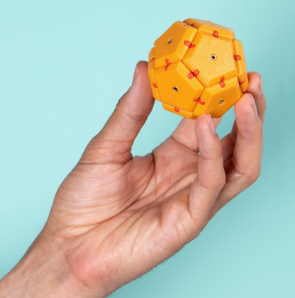 Hand holding a yellow dodecahedron-shaped fidget toy against a light blue background