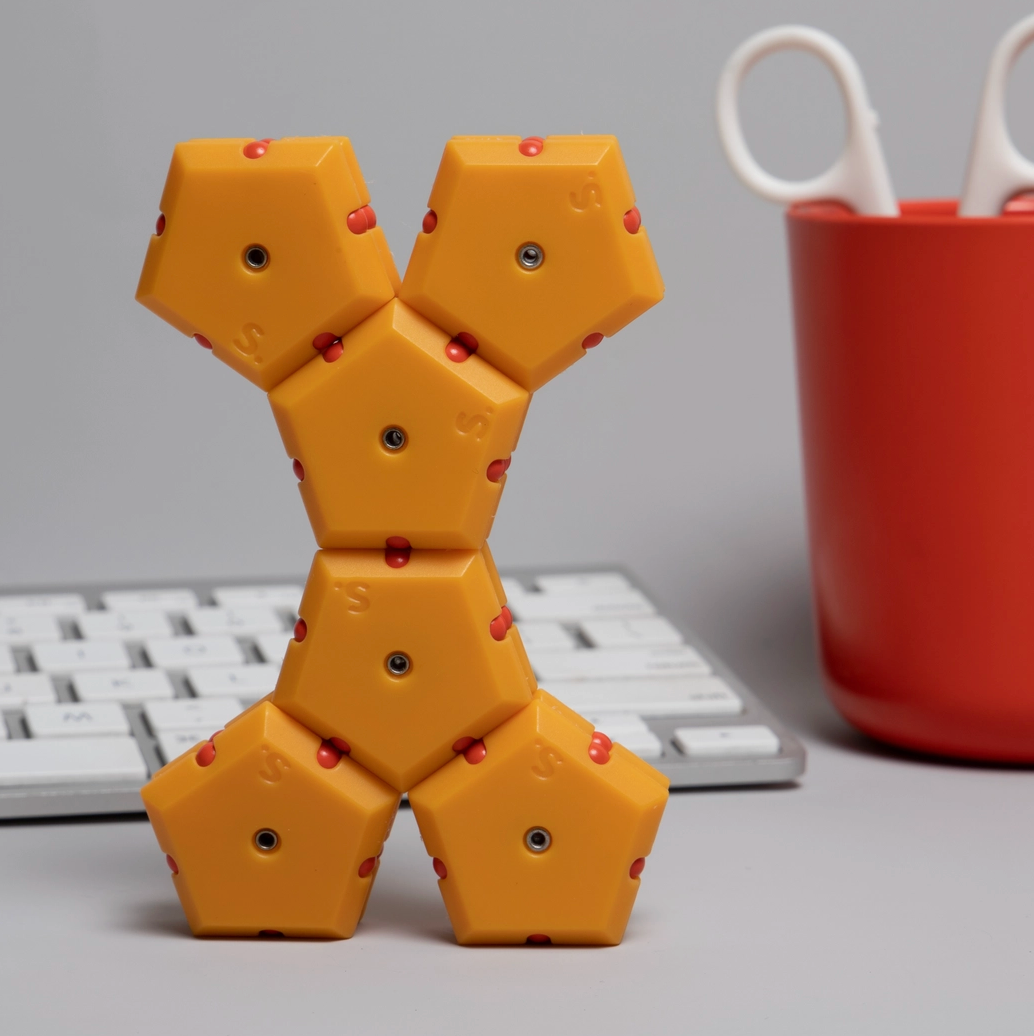 Yellow geometric puzzle toy on a desk with a red cup and white scissors in the background.