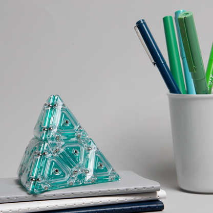 Geometric pyramid decoration on a stack of books with pens in the background