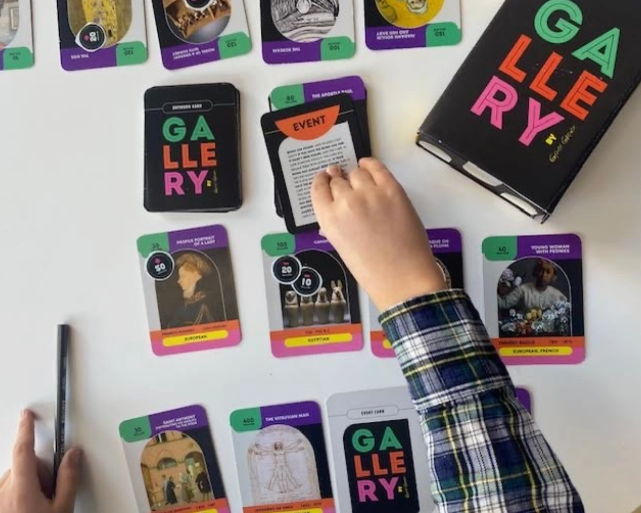 Person playing a card game with 'GALLERY!' cards on a white surface.