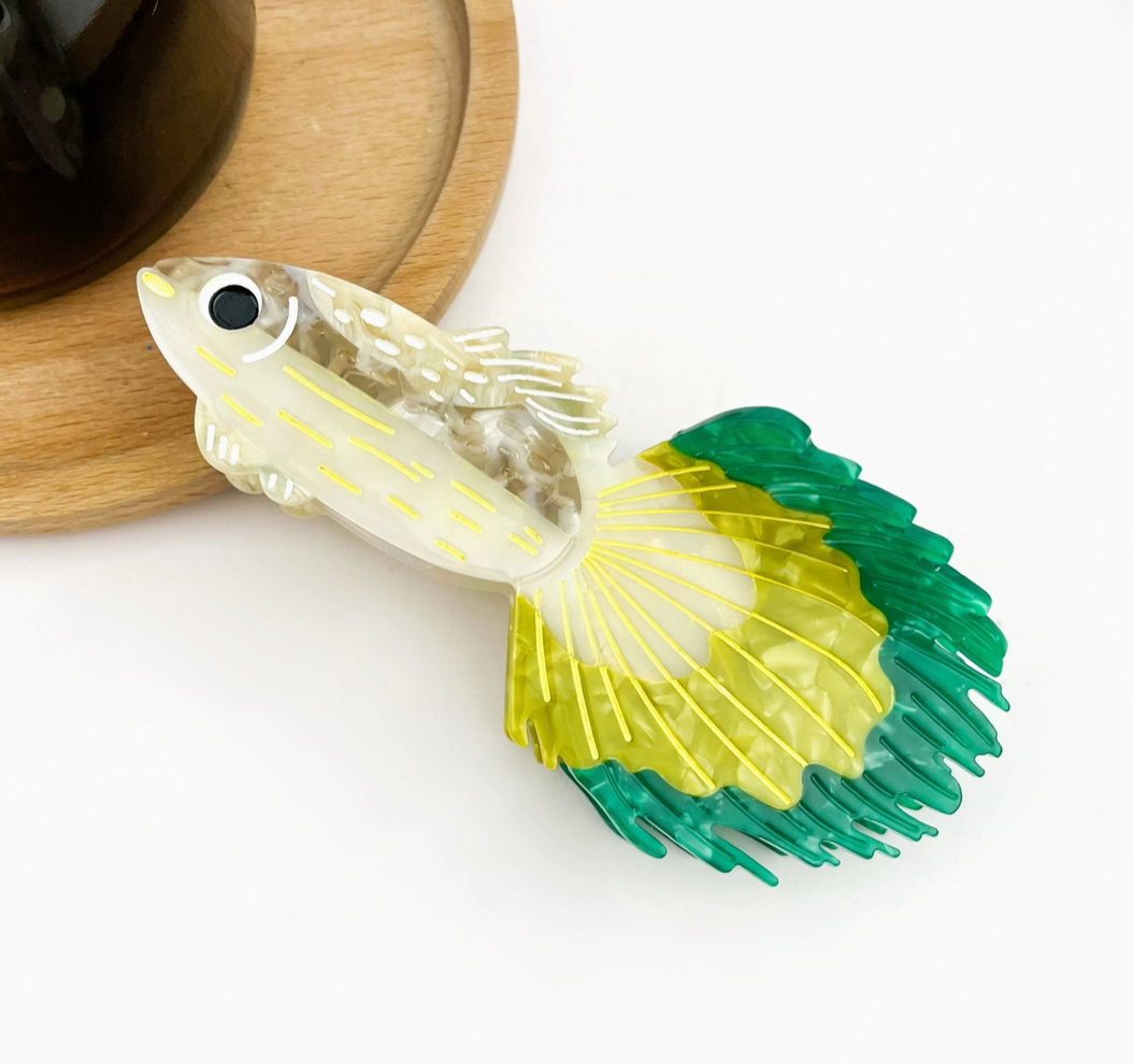 Decorative fish-shaped hair clip with green and yellow tail on a white background.