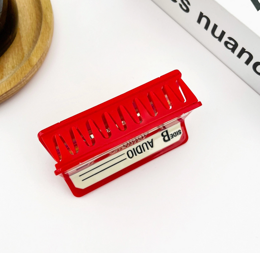 Red cassette tape hair clip with 'Audio' label on a white background.