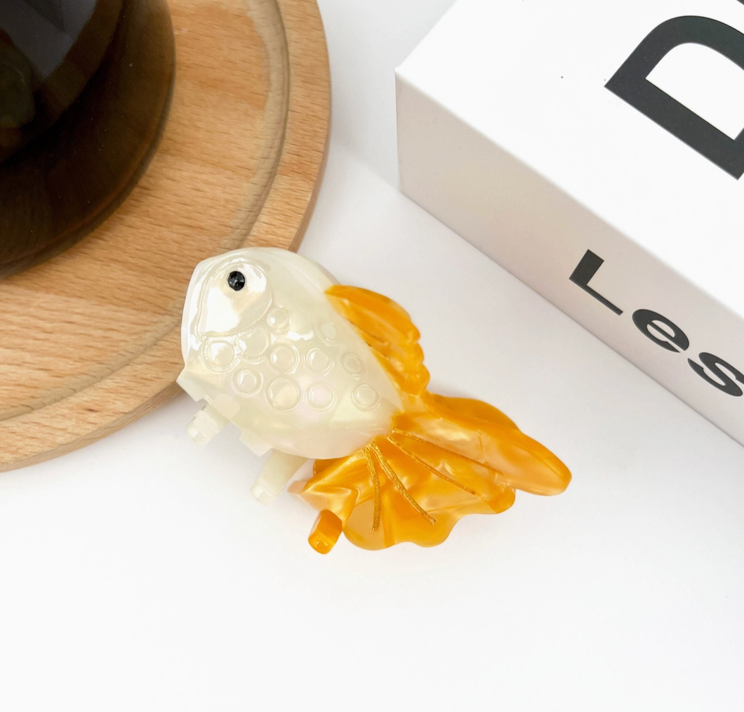 Decorative goldfish hair clip on a white surface with a book in the background.