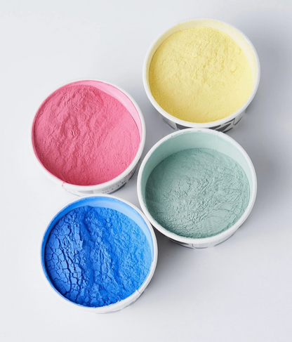Four bowls with pink, yellow, blue, and green powders on a light gray background.