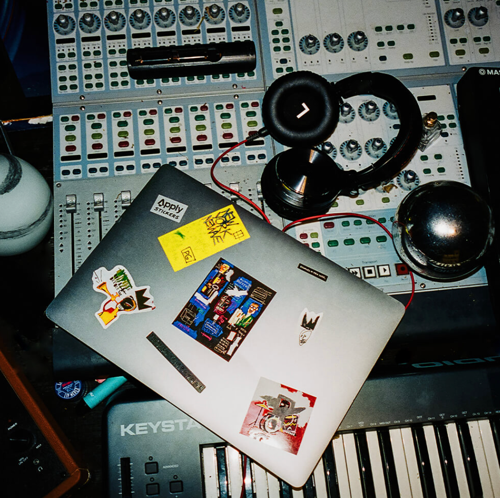 Laptop with stickers on a music production setup with headphones and equipment.
