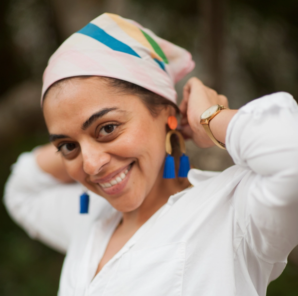 Woman wearing a colorful headscarf and white shirt with blue earrings.