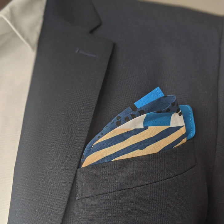 Blue and beige striped pocket square in a dark gray suit jacket pocket.