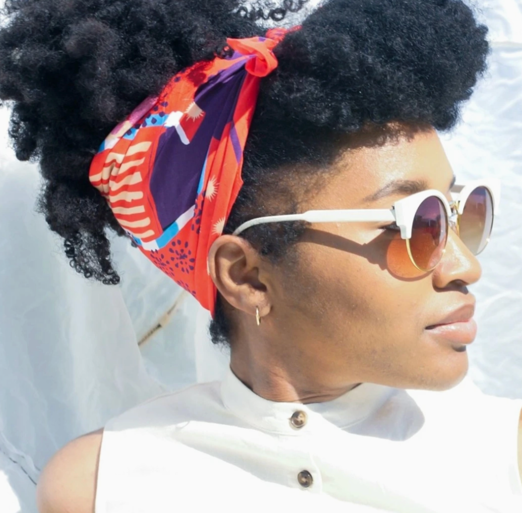 Person wearing a colorful headscarf and sunglasses with a white background