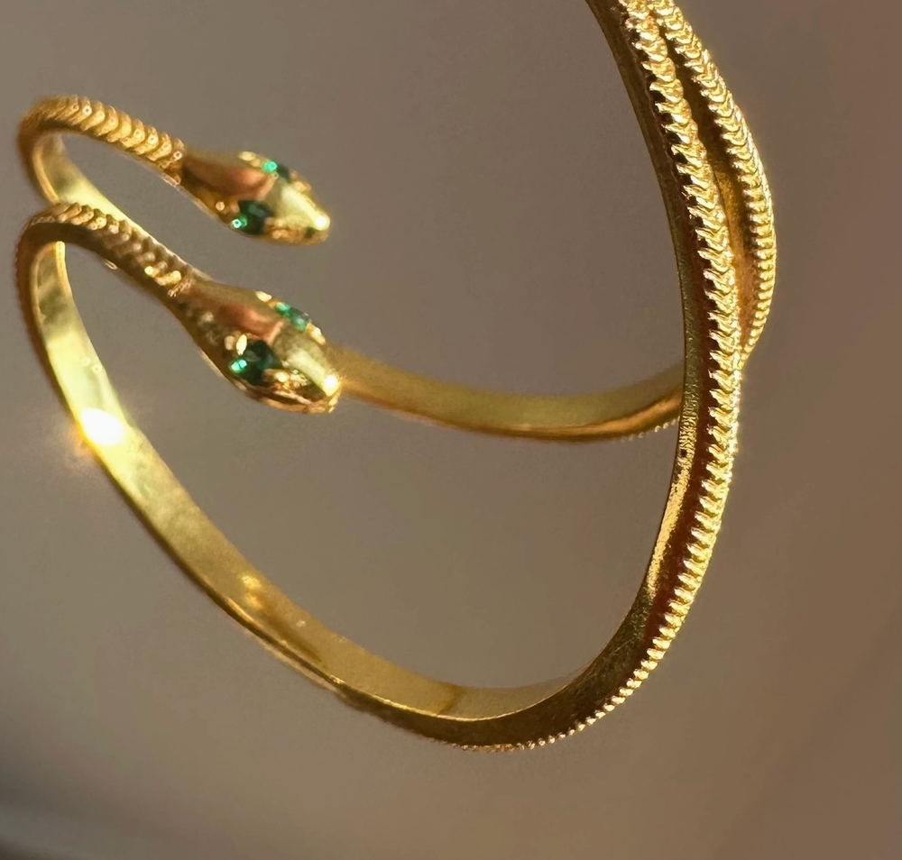 Gold snake-shaped hoop earrings on a plain background.