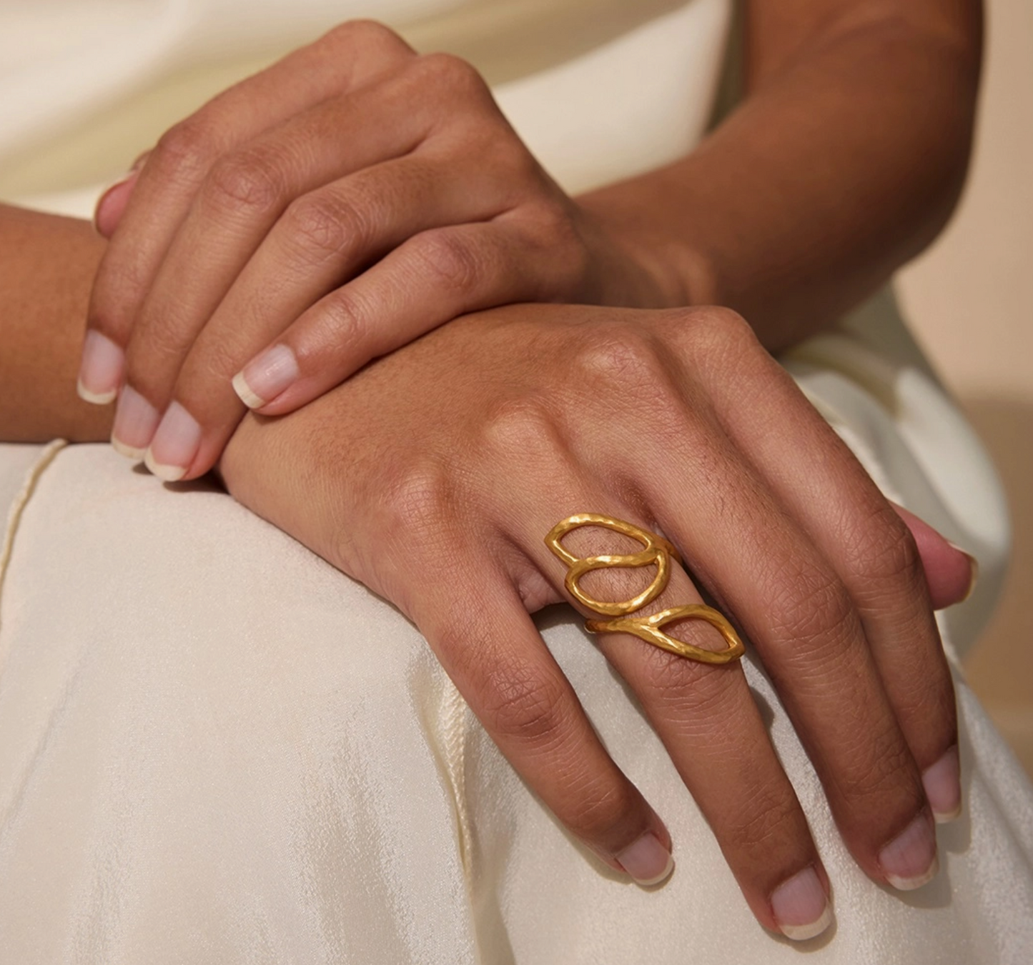 Close-up of a hand wearing a gold ring on a neutral background