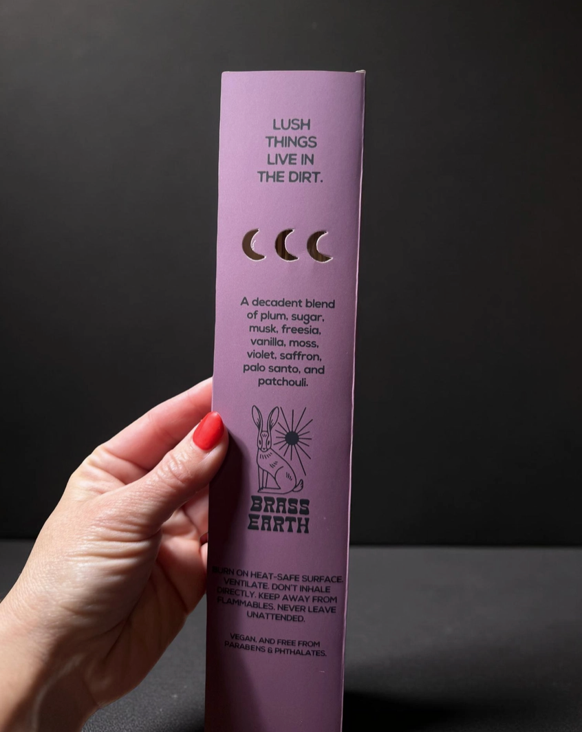 Hand holding a purple Lush product packaging against a dark background
