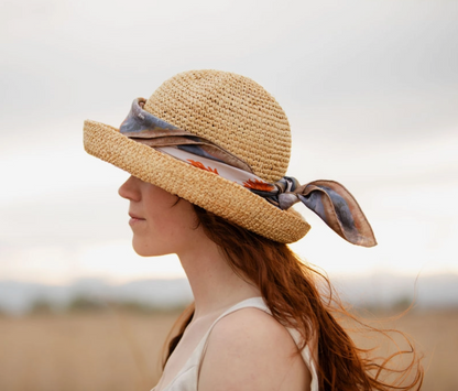 Woman wearing a straw hat with a scarf standing against a blurred natural background