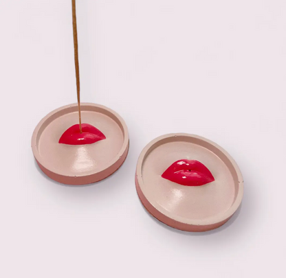 Two concrete incense holders with red lip designs on a white background