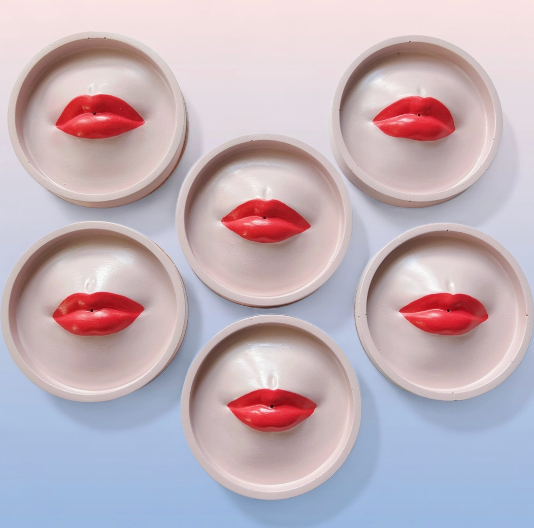 Soft pink red lip-shaped incense holders on a light blue background