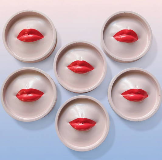 Soft pink red lip-shaped incense holders on a light blue background
