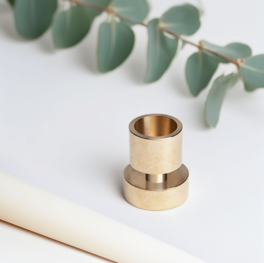 Brass candle holder on a white surface with green leaves in the background