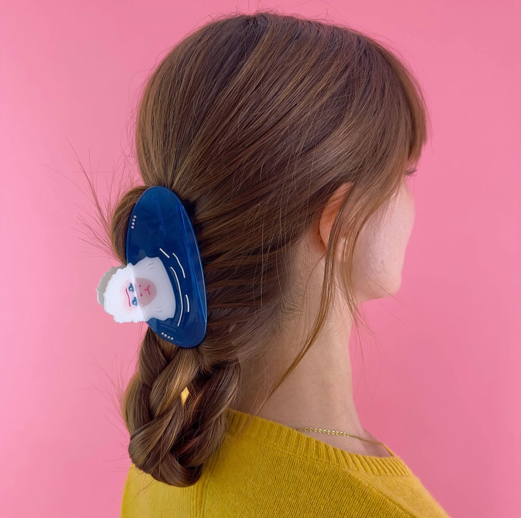 Person with a braid wearing a blue hair hair clip against a pink background