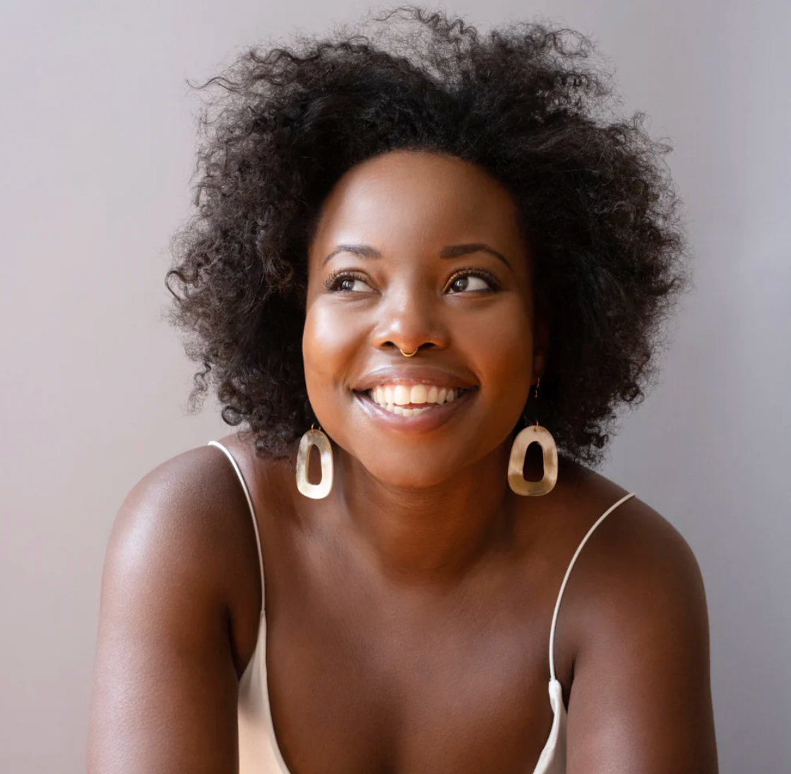 Woman with curly hair wearing hoop earrings against a neutral background