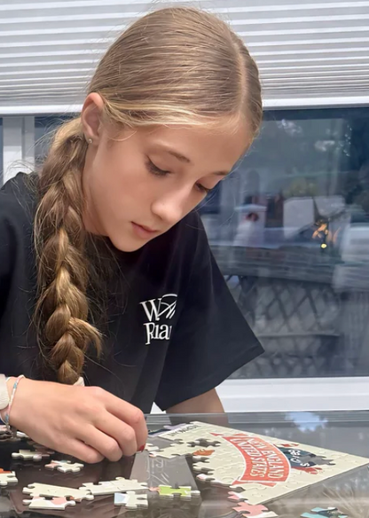 Young girl with braided hair working on a puzzle at a table.