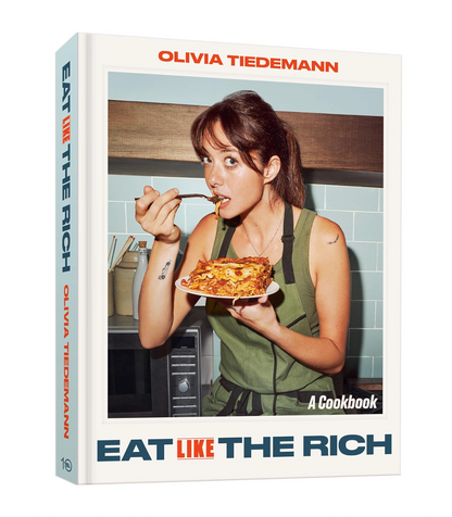 The front and spine of the cookbook 'Eat Like The Rich' by Olivia Tiedemann, featuring a photo of a woman eating pizza in a kitchen on the cover.