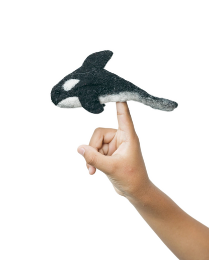 Hand holding a felt orca whale toy against a white background