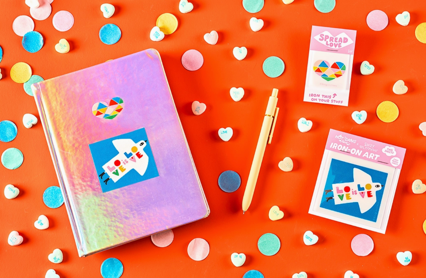 Colorful notebook, pen, and ion-on decals on an orange background with heart-shaped confetti.