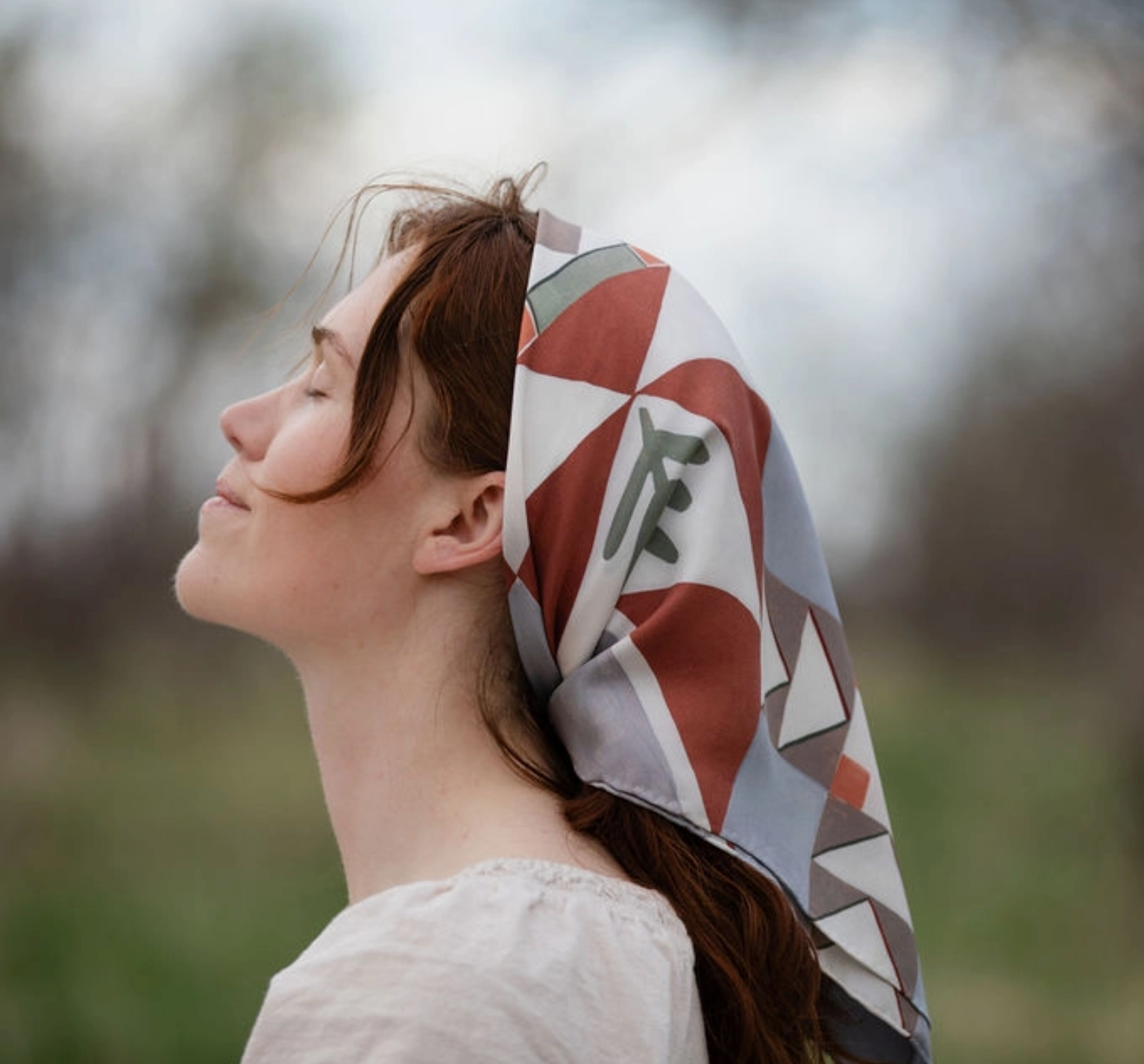 Woman wearing a patterned headscarf outdoors with a blurred natural background
