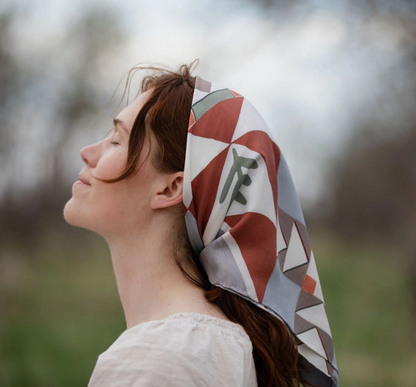 Woman wearing a patterned headscarf outdoors with a blurred natural background