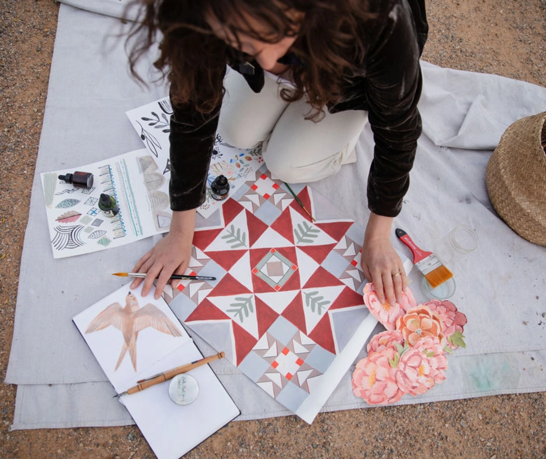 Person working on a quilt with various designs and tools on a blanket outdoors.