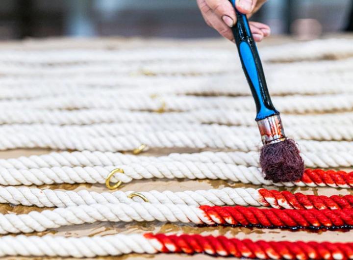 Person using a brush to paint red details on a rope surface