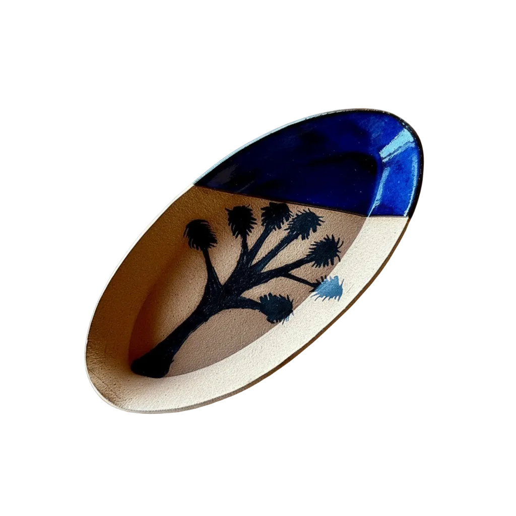 A handcrafted oval tray made from a natural wood slice, featuring a black painted Joshua tree design and a glossy deep blue top section, displayed on a woven jute mat.