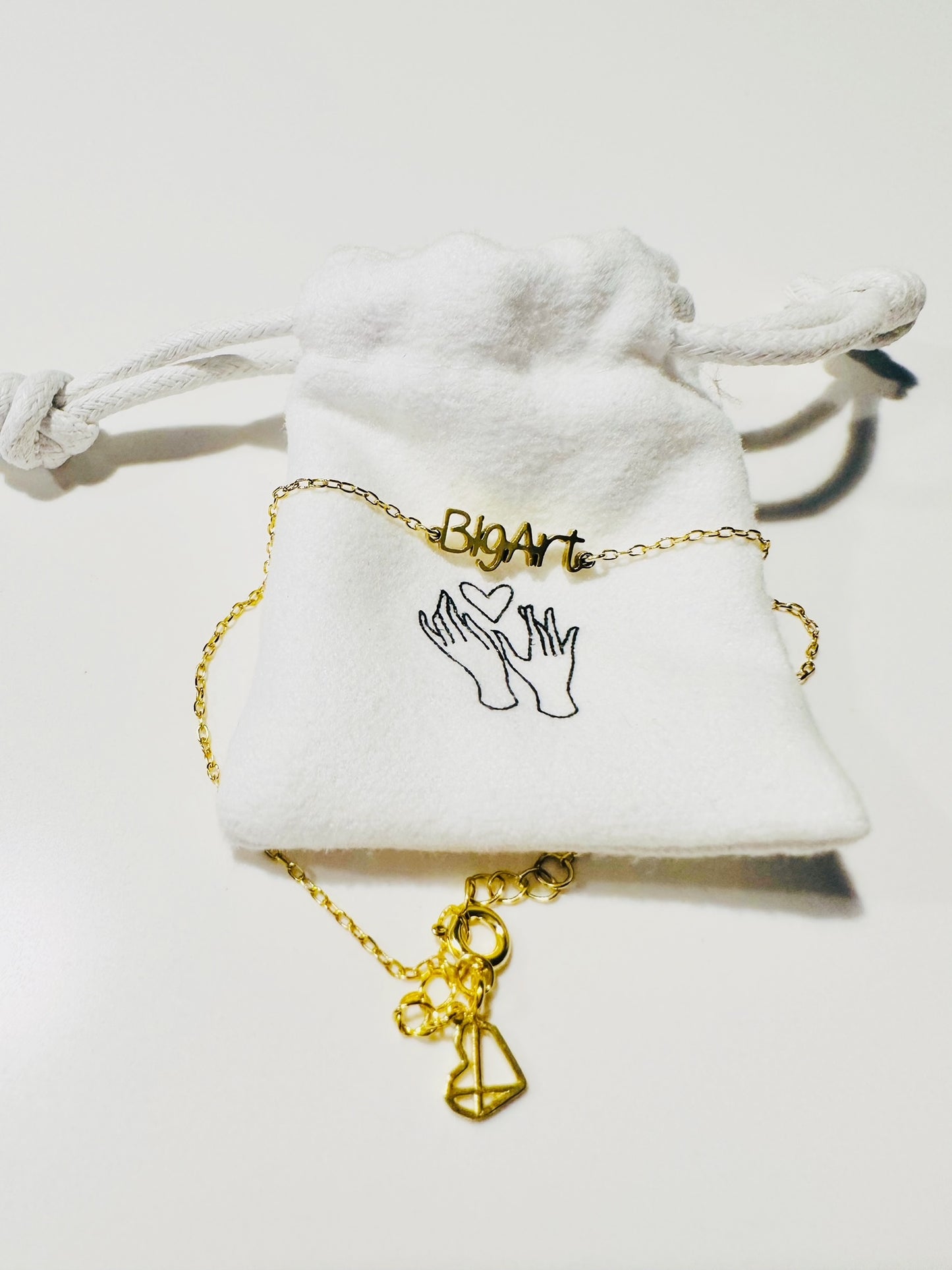 Delicate chain with a with a word charm reading ’BigArt’ with fabric bag packaging 

