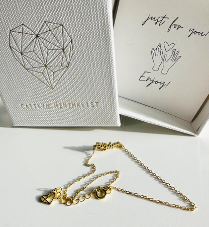 Delicate chain with a with a word charm reading ’BigArt’ next to box packaging